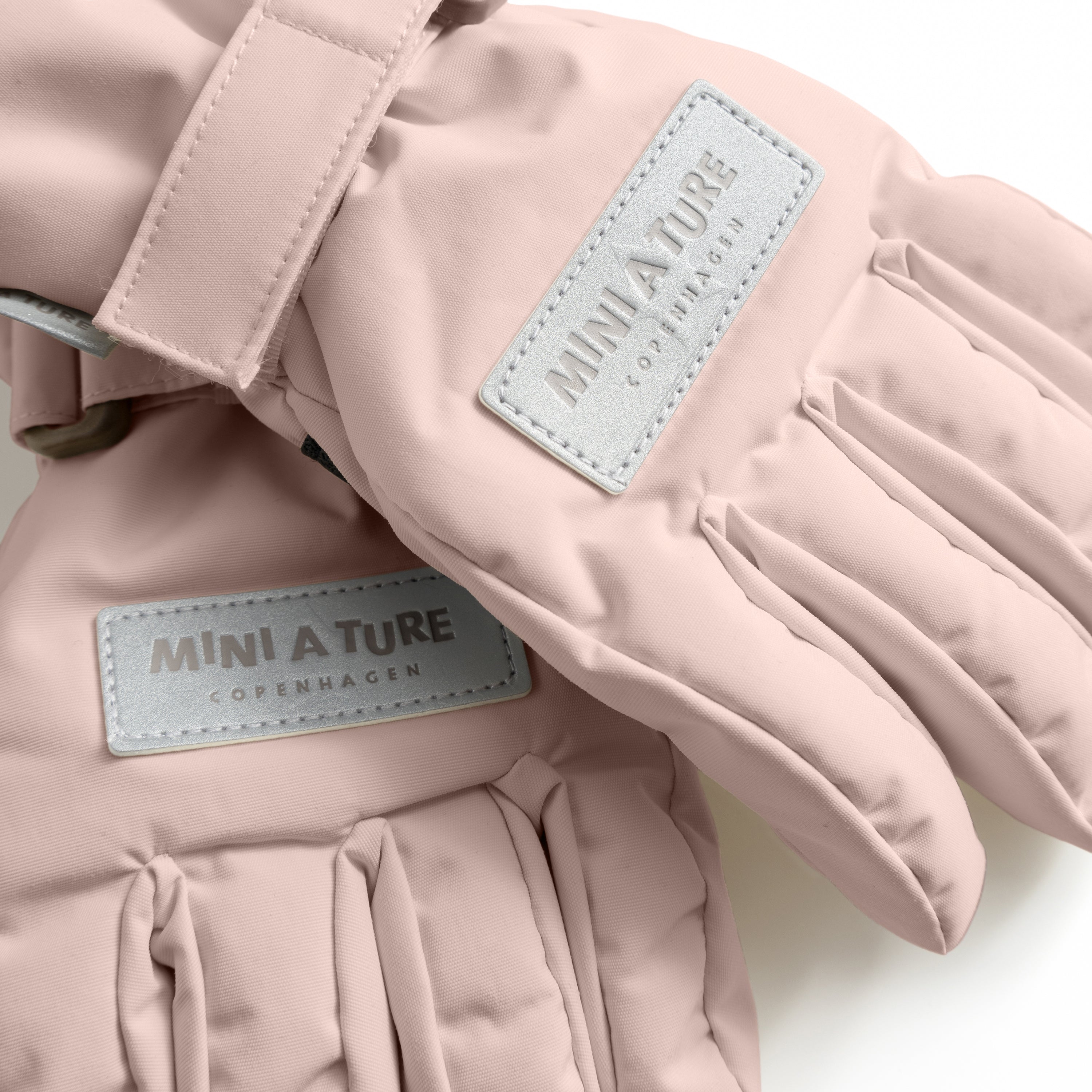 MATCELIO gloves in soft pink with embossed MINI A TURE Copenhagen label on the back of hand, adjustable wrist strap with buckle closure and extended cuff, photographed in close-up against a white background.