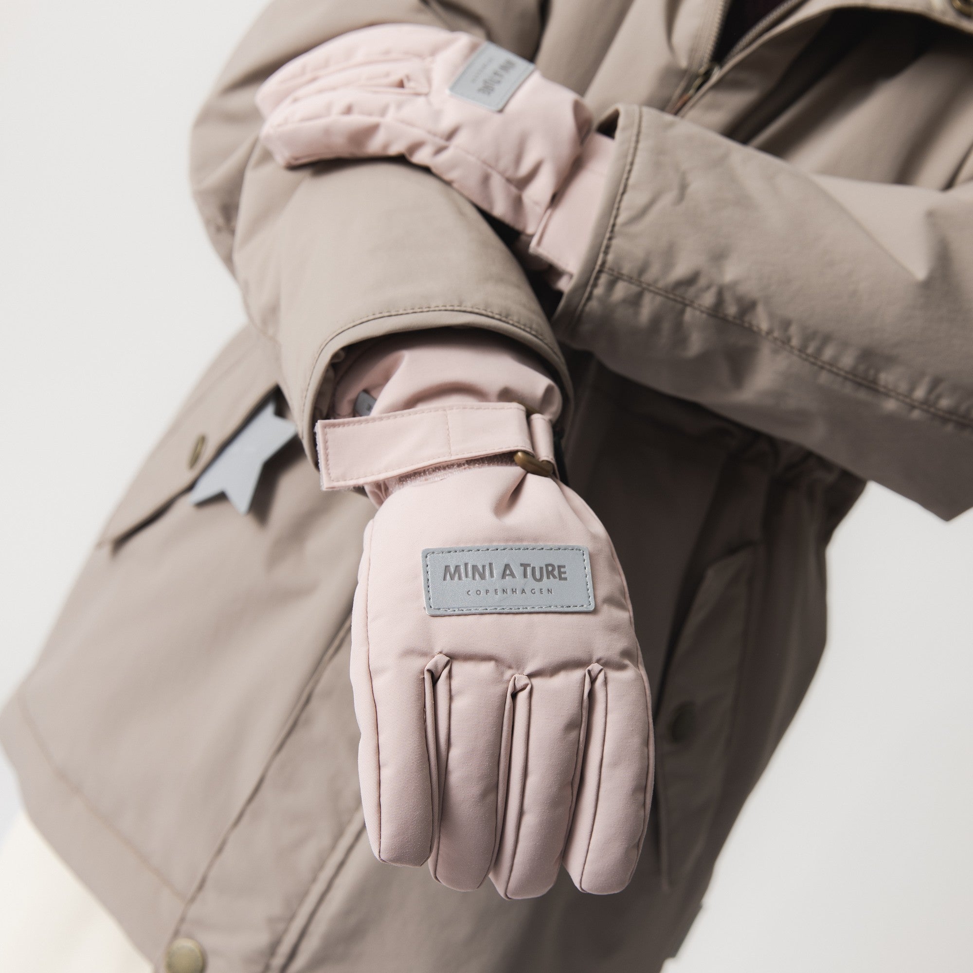 MATCELIO gloves in soft pink worn with a matching winter jacket, showing the extended cuff sealing the gap between sleeve and glove, with MINI A TURE Copenhagen label visible on the back of hand.