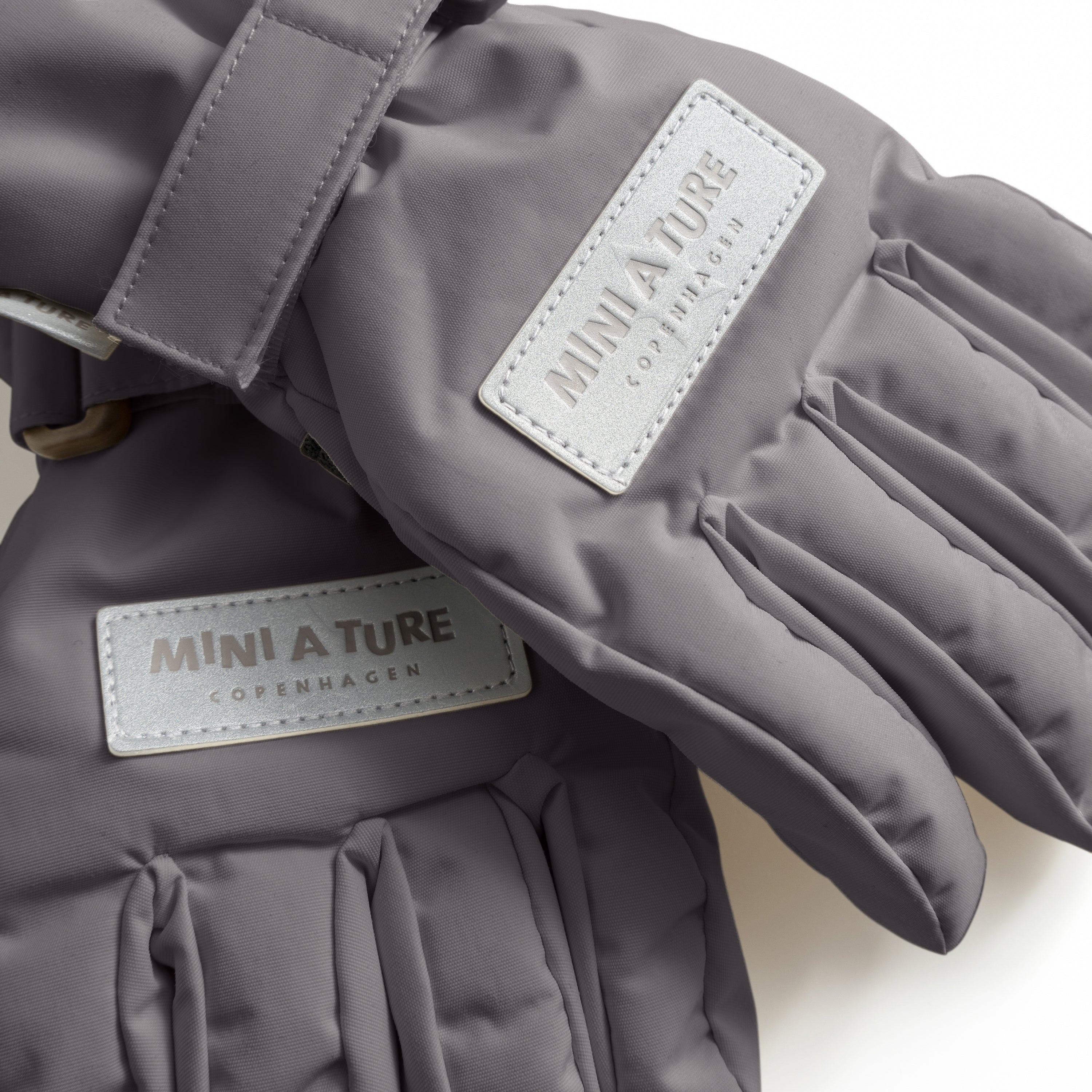 MATCELIO waterproof gloves in grey featuring embossed MINI A TURE Copenhagen branding on the back of hand, photographed in close-up to show THERMOLITE padding and recycled nylon construction.