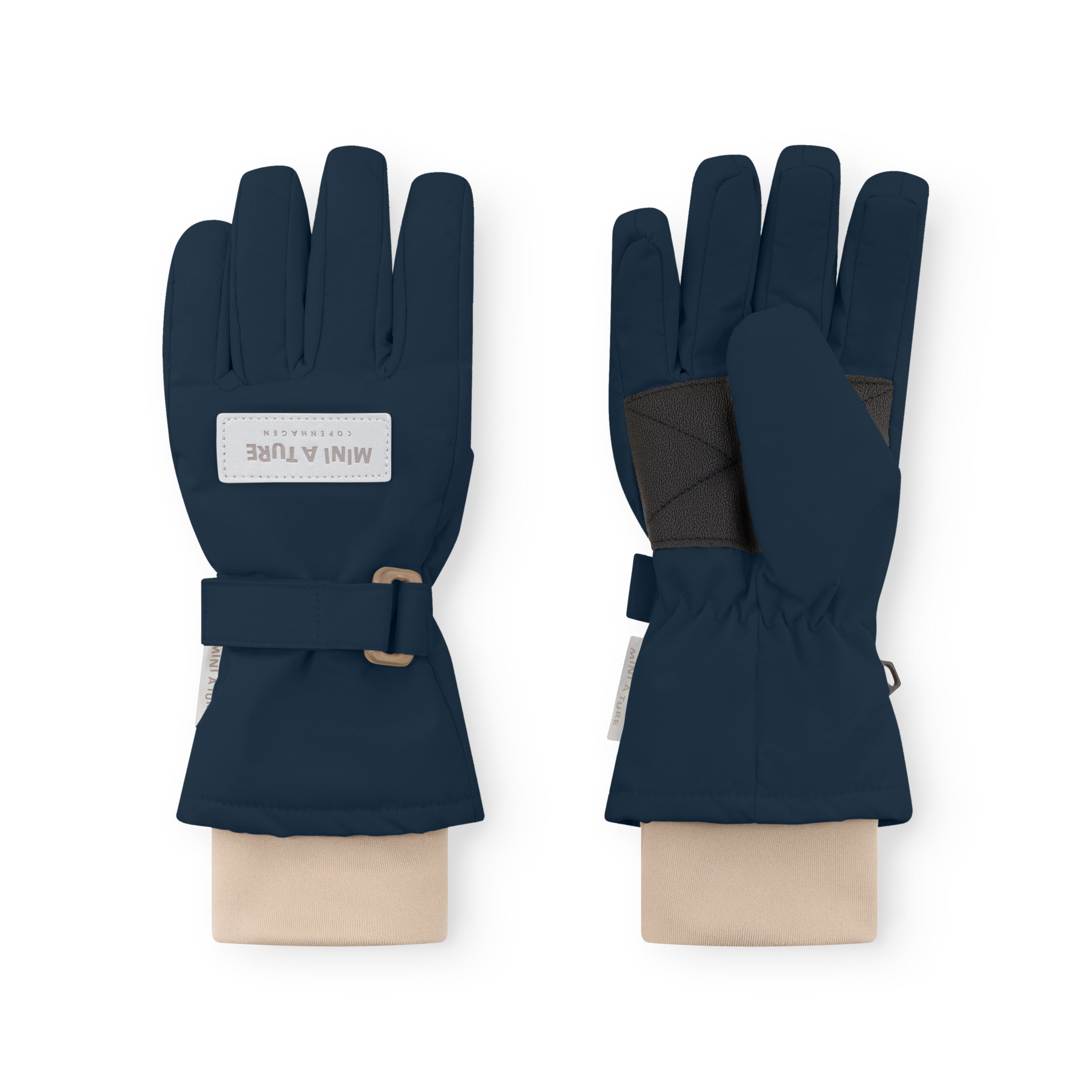 MATCELIO gloves in deep navy blue displayed on neutral fabric wrists, showing both palm and back views with the white embossed MINI A TURE Copenhagen label on the back of hand, black elasticated internal wrist cuff visible beneath the extended cuff, and the adjustable buckle strap fastened on the outer cuff.
