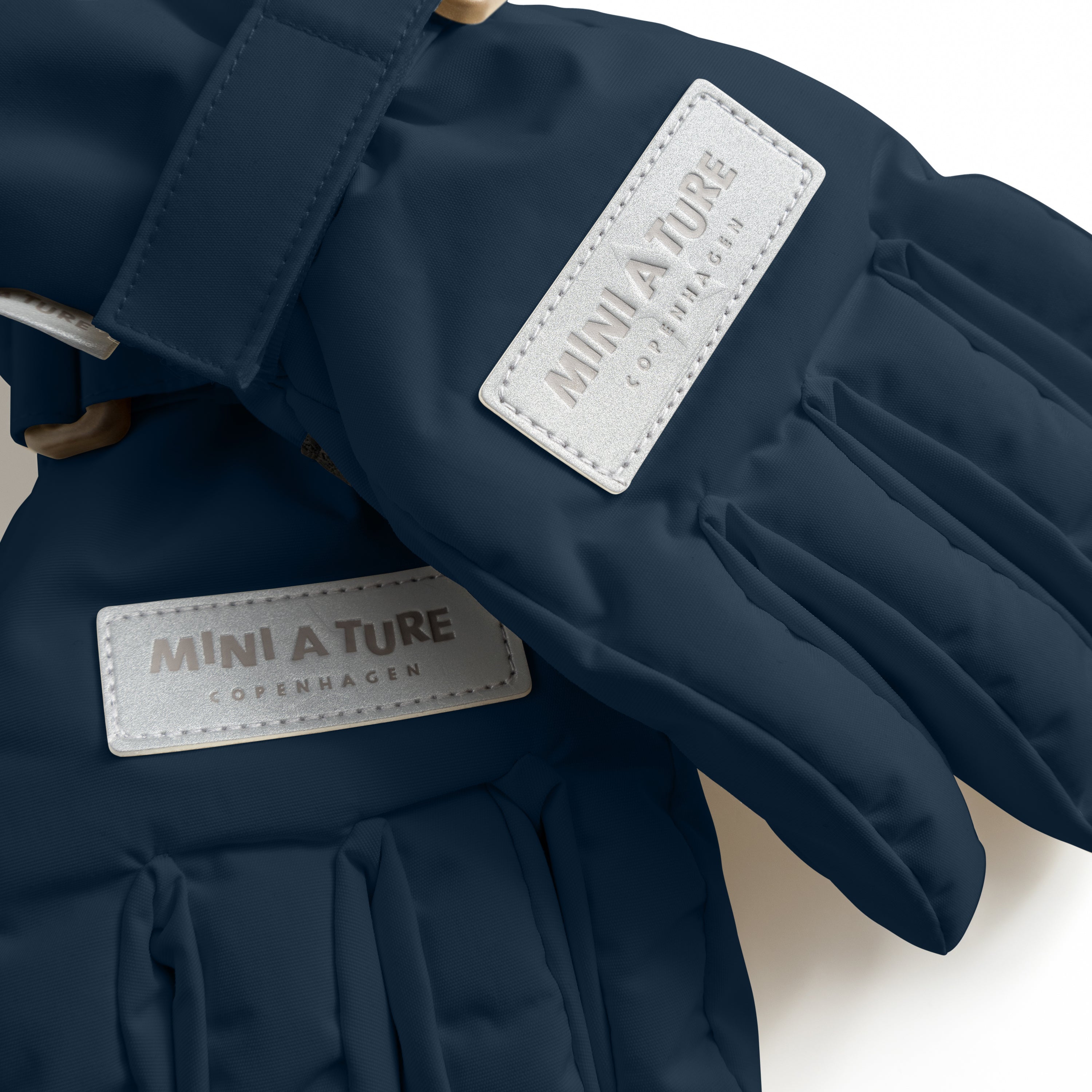MATCELIO gloves in deep navy blue with white embossed MINI A TURE Copenhagen labels on both the back of hand and extended cuff, photographed flat to show the waterproof recycled nylon outer shell, THERMOLITE padding construction and adjustable wrist strap with buckle closure.