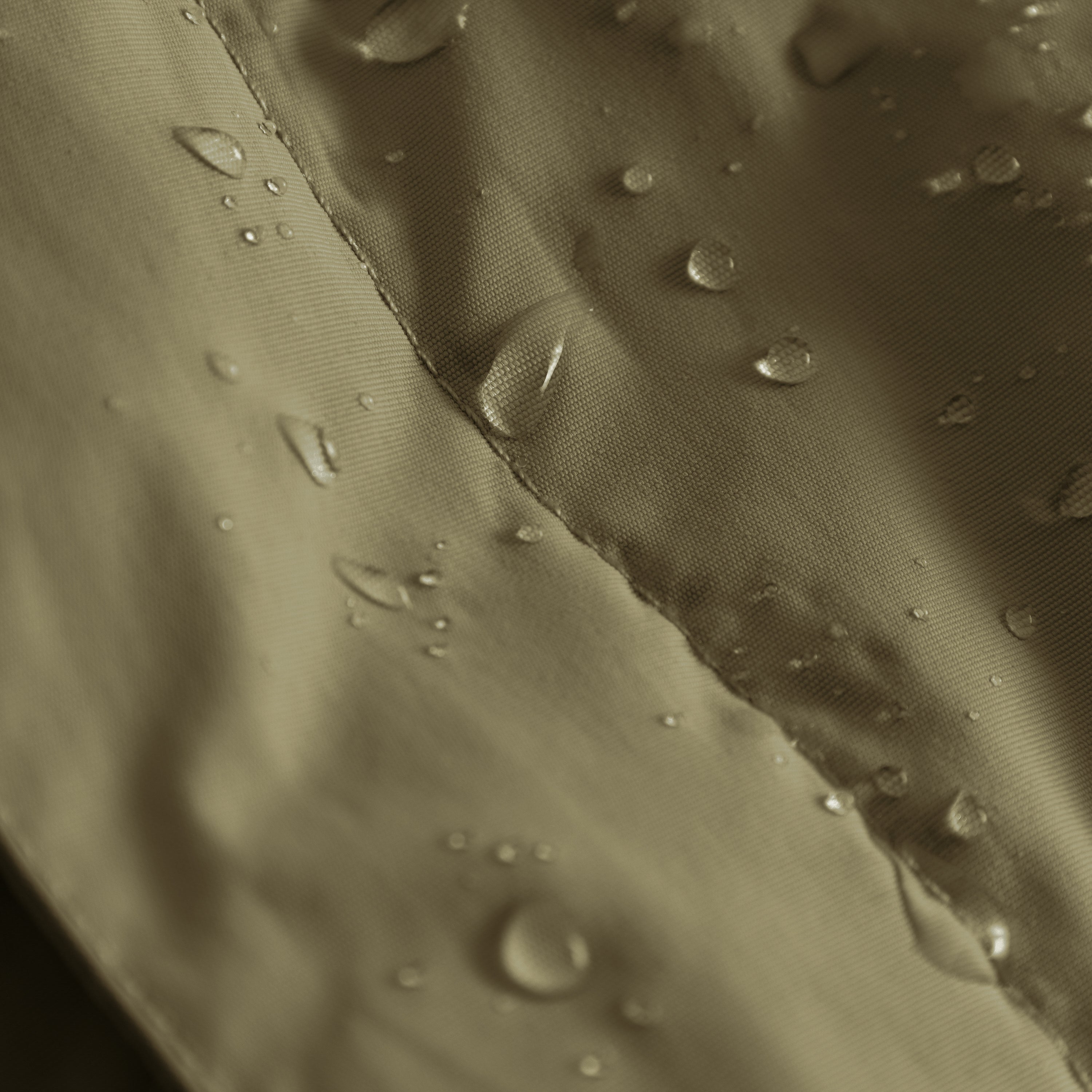 MATBABYWEN anorak in olive green showing water droplets beading on the fluorine-free Bionic Finish Eco treated recycled polyamide shell, with a close-up view of the fully taped seam construction demonstrating waterproof performance.