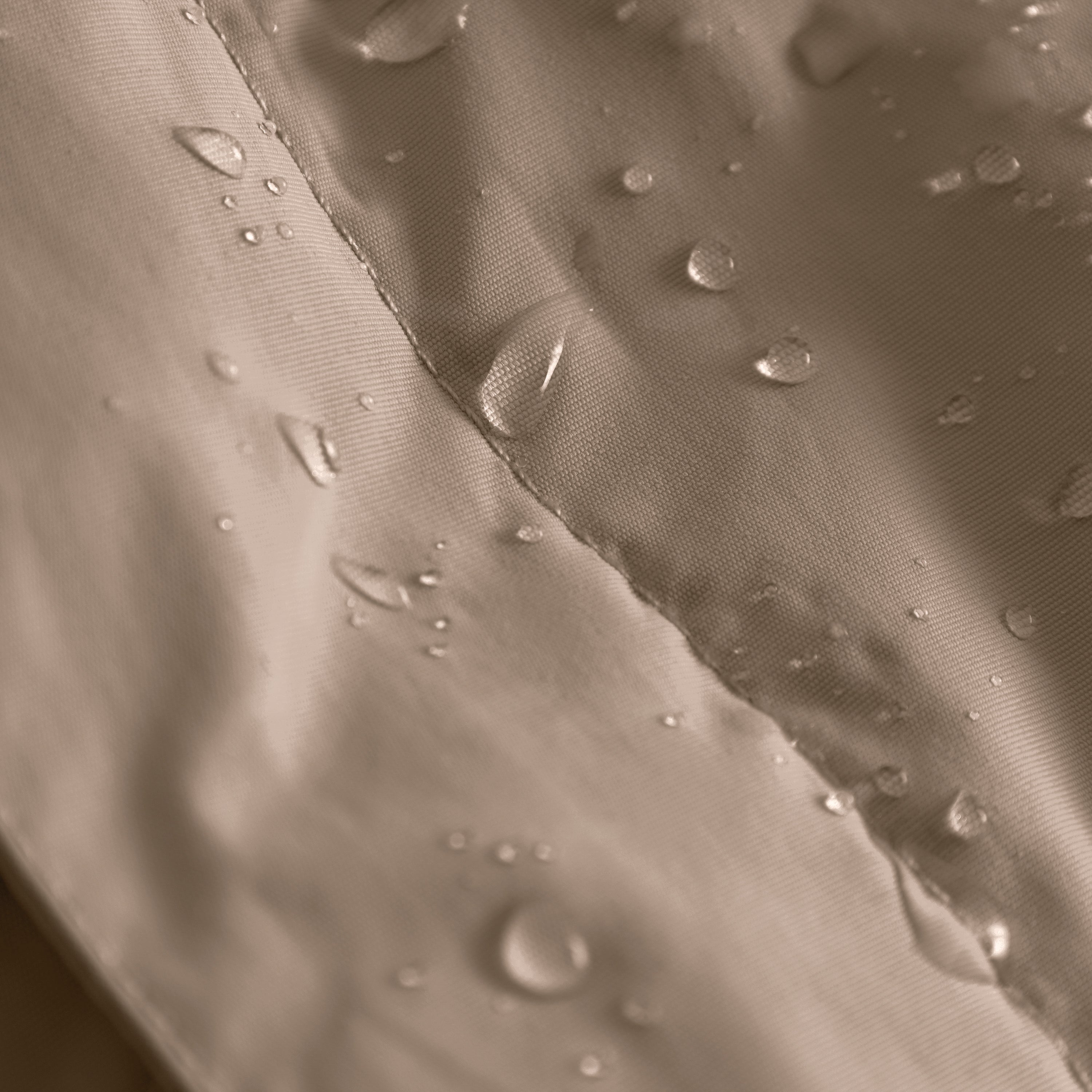 MATBABYWEN anorak in soft beige showing water droplets beading on the recycled polyamide outer shell treated with fluorine-free Bionic Finish Eco, with a close view of the fully taped seam construction running diagonally across the 12,000mm waterproof-rated fabric.