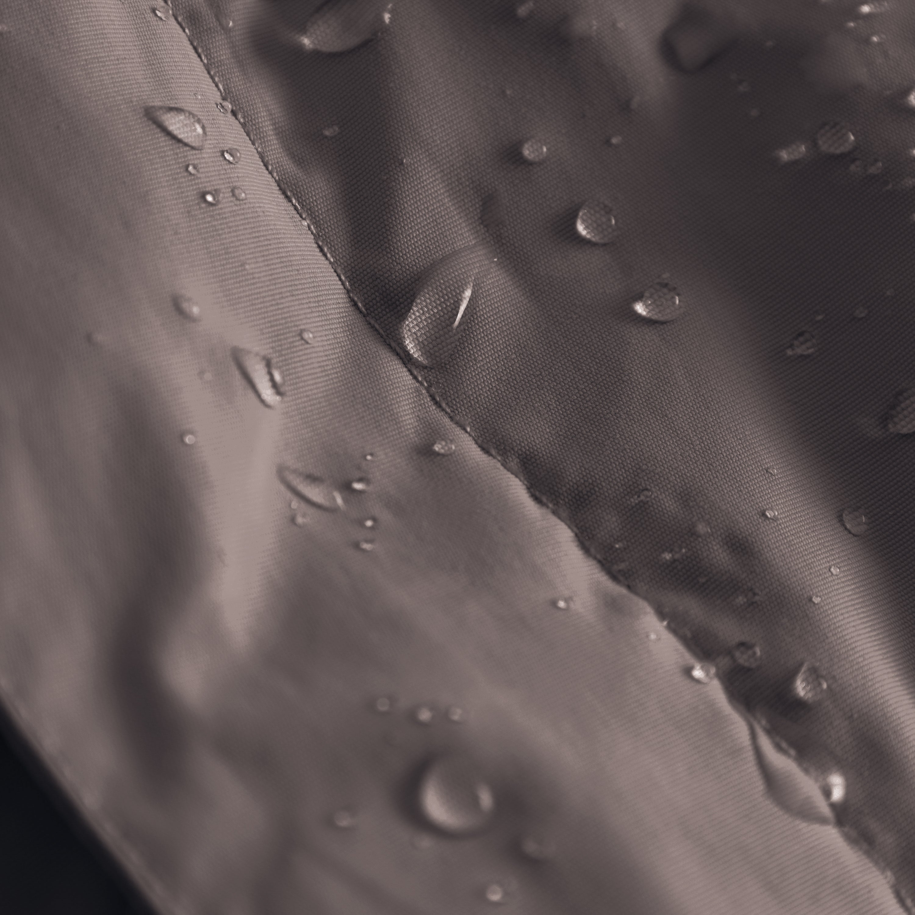 MATBABYWEN anorak in grey showing water droplets beading on the fluorine-free Bionic Finish Eco treated surface, with a close-up view of the taped seam and the textured recycled polyamide shell fabric demonstrating water-repellent performance.