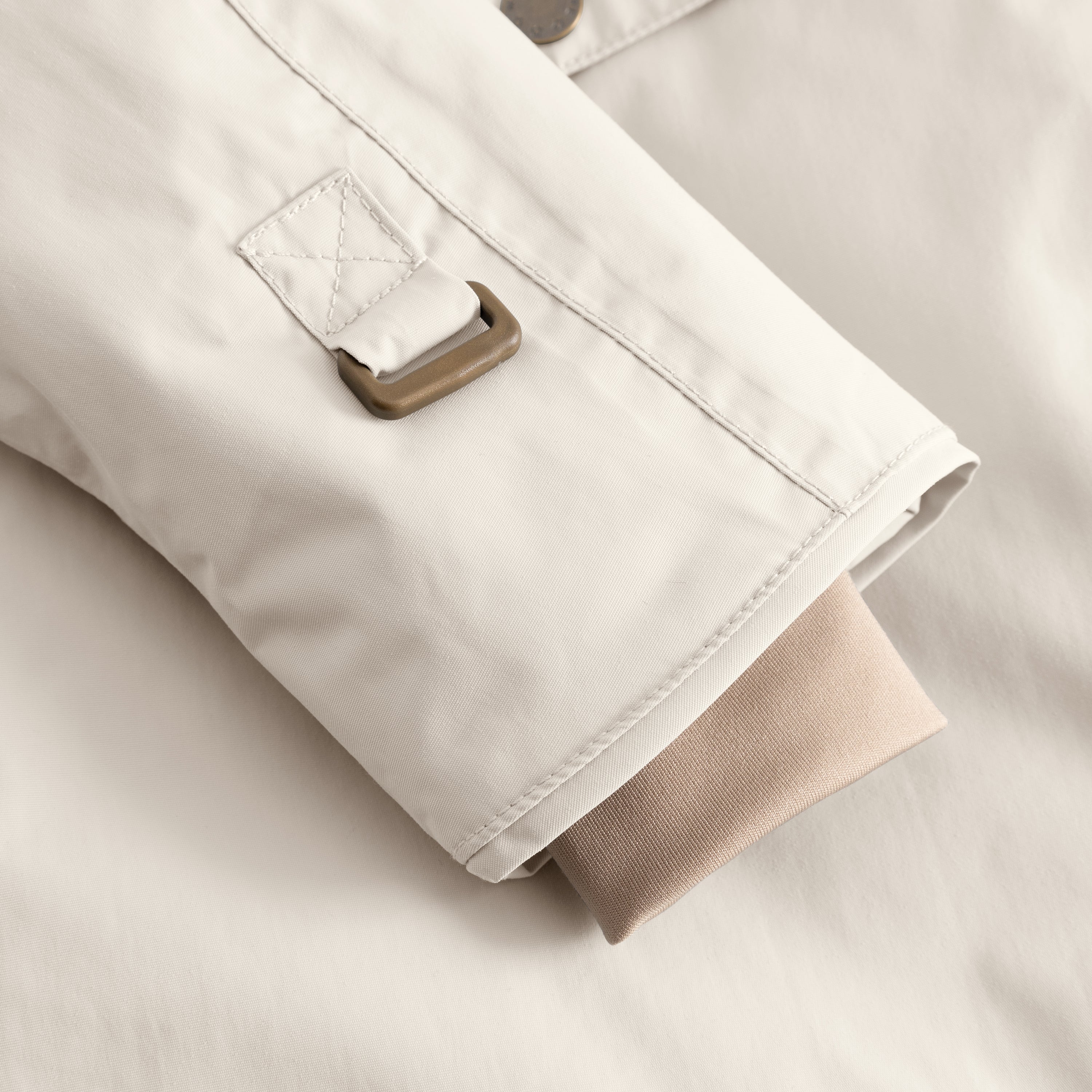 Close-up of the MATWANG fleece-lined winter jacket's left sleeve showing the bronze D-ring buckle fastening system with quilted fabric tab, flat-felled seam construction, and the soft beige ribbed knit inner cuff extending from the sleeve opening to provide a snug seal at the wrist.