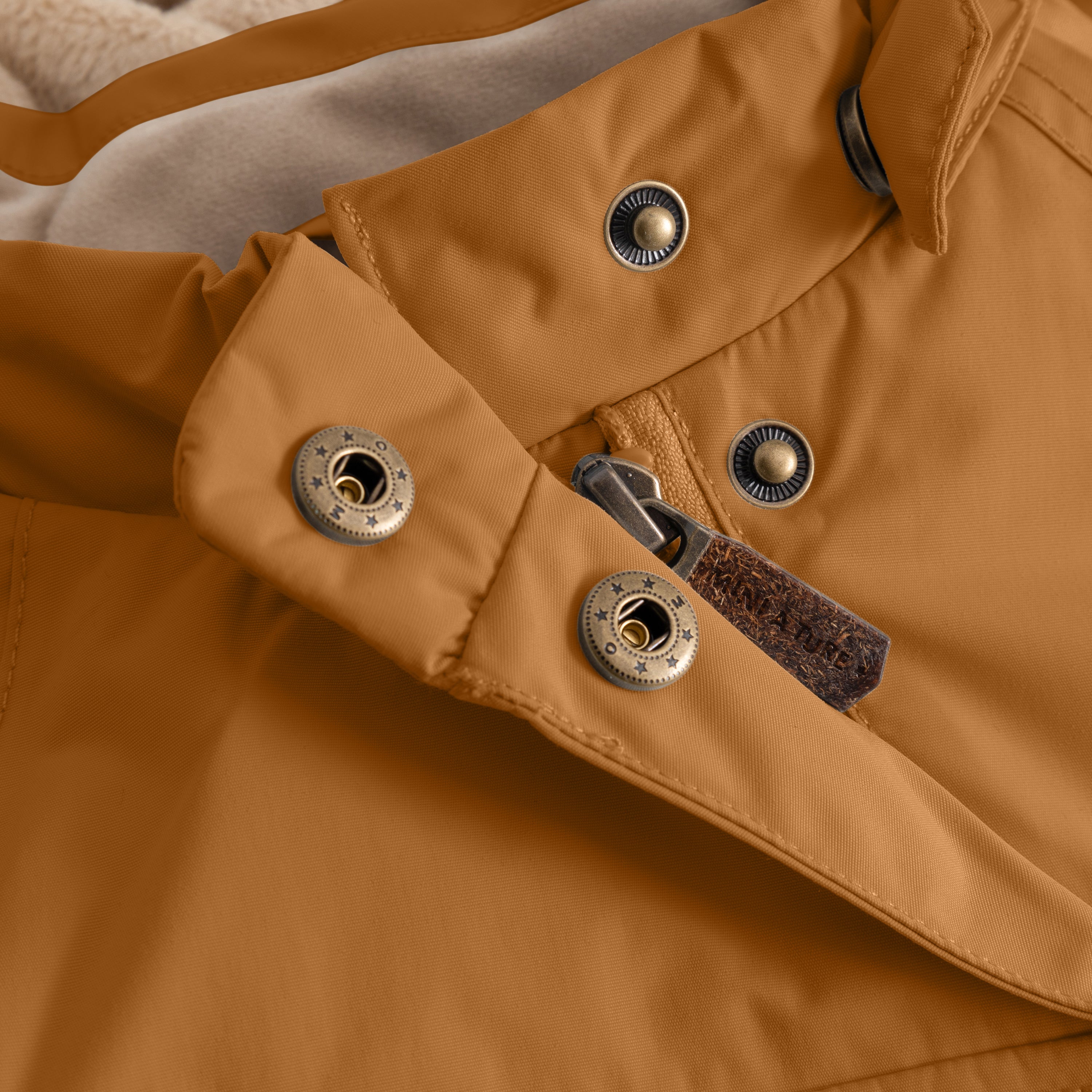 Detail of the MATWANG fleece-lined winter jacket's left sleeve cuff showing the bronze-toned metal D-ring fastening, bronze press studs securing the adjustable snow cuff with thumb opening, and beige fleece lining visible at the wrist edge.