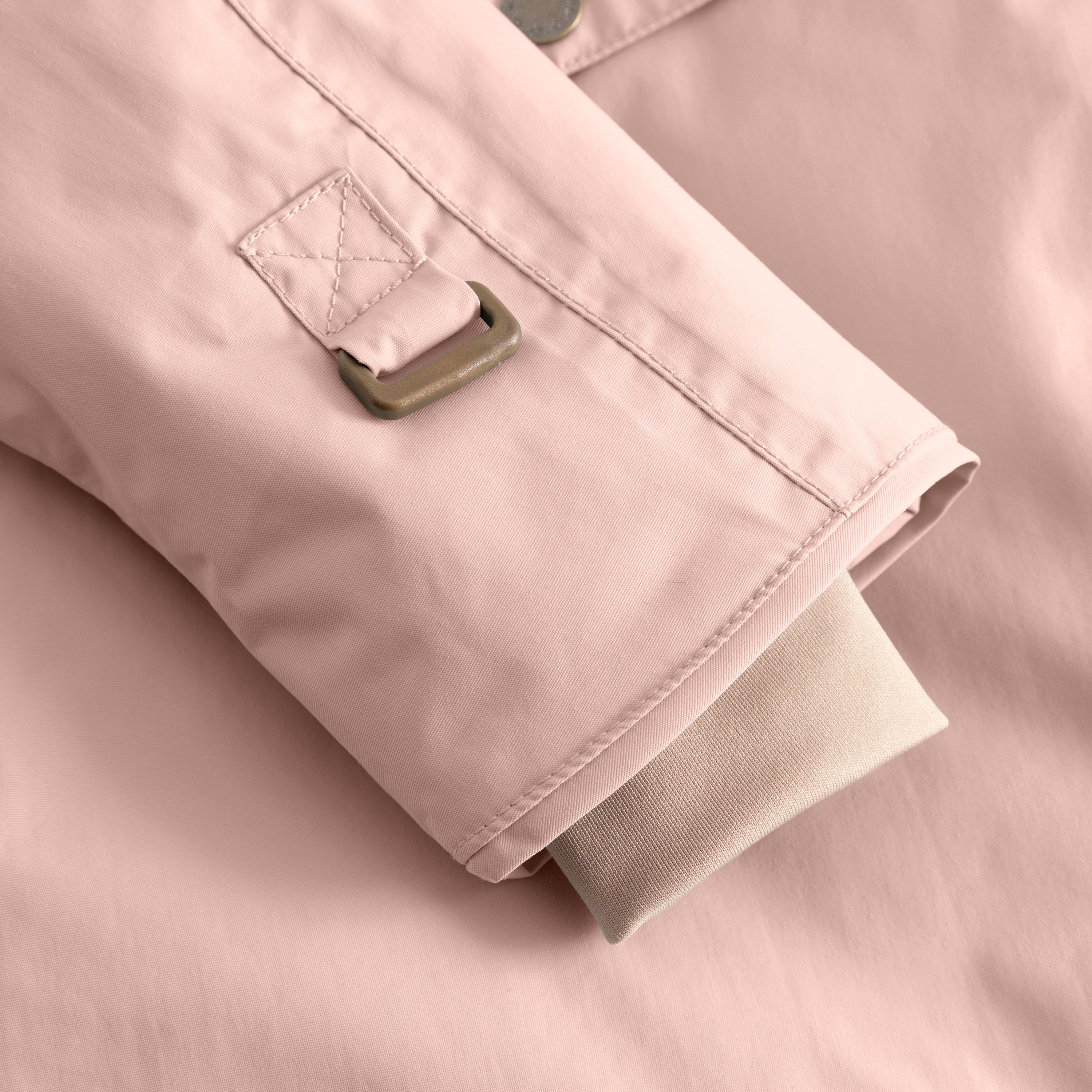 Close-up of a pale pink children's winter jacket sleeve cuff with an adjustable strap and metal buckle, showing ribbed inner cuff detail and waterproof outer fabric construction.