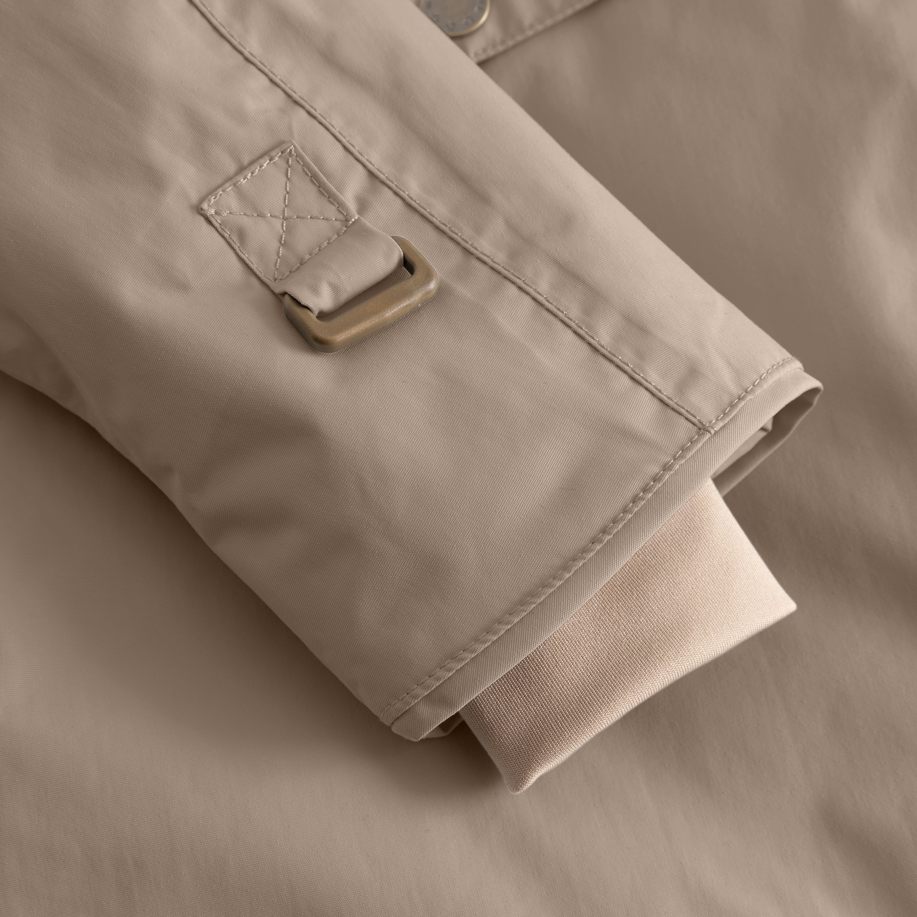 Close-up of a beige children's winter jacket sleeve cuff showing an adjustable tab with metal buckle and ribbed inner cuff for secure fit and weather protection.
