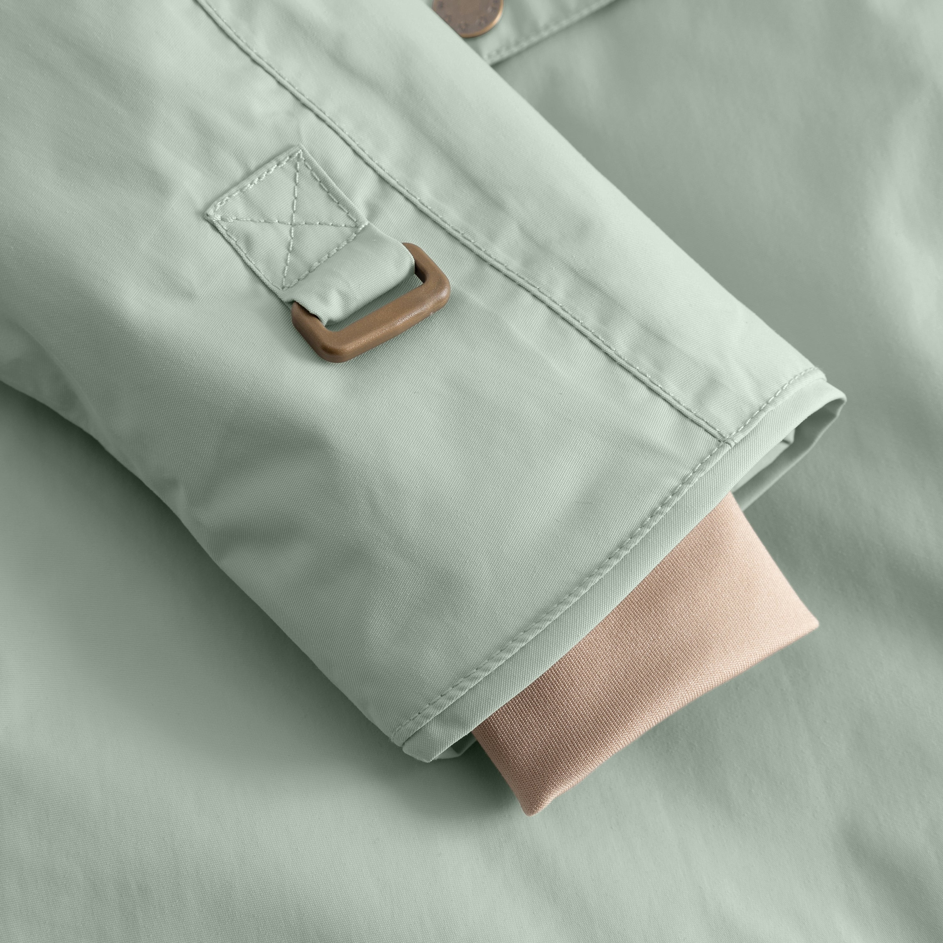Detail of the MATWANG fleece-lined winter jacket's internal snow cuff showing the bronze-toned D-ring buckle fastening, flat-felled seam construction, and soft pink ribbed knit inner cuff extending from the sleeve opening to seal the gap between jacket and glove.