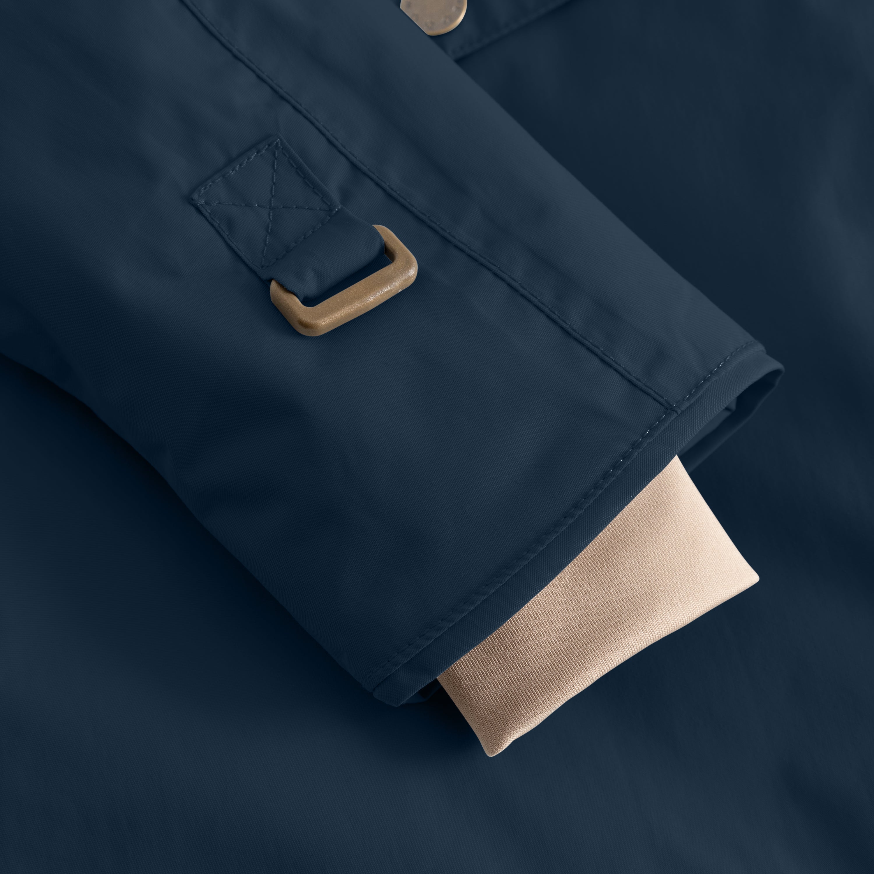 Close-up of a children's winter jacket sleeve in deep blue recycled nylon, showing a star-embossed pocket flap with a wooden toggle closure and a beige ribbed inner cuff extending from the hem.