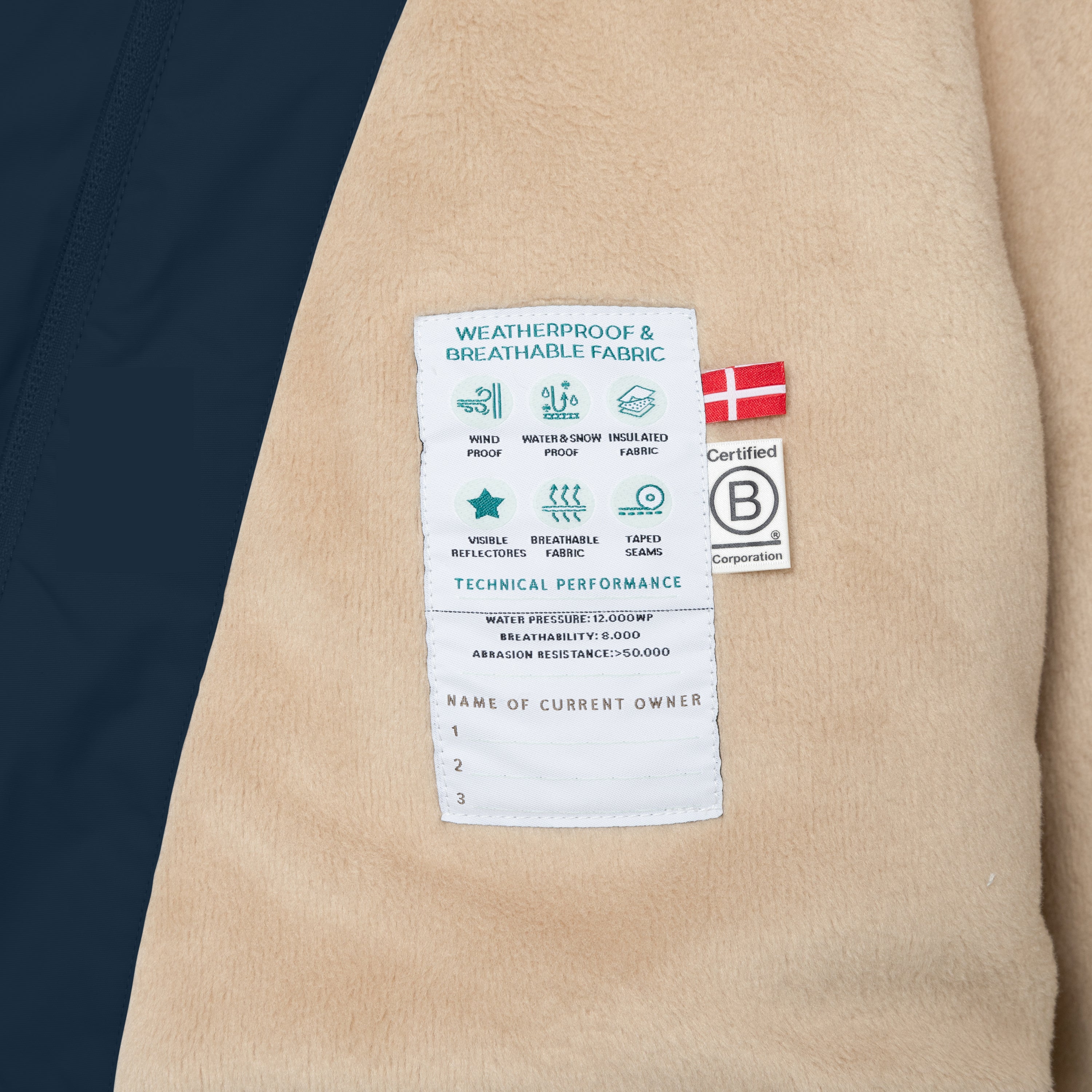 Fleece-lined kids' winter jacket in beige with a technical performance label showing windproof, waterproof and breathable fabric specifications, alongside a Danish flag and B Corporation certification badge.