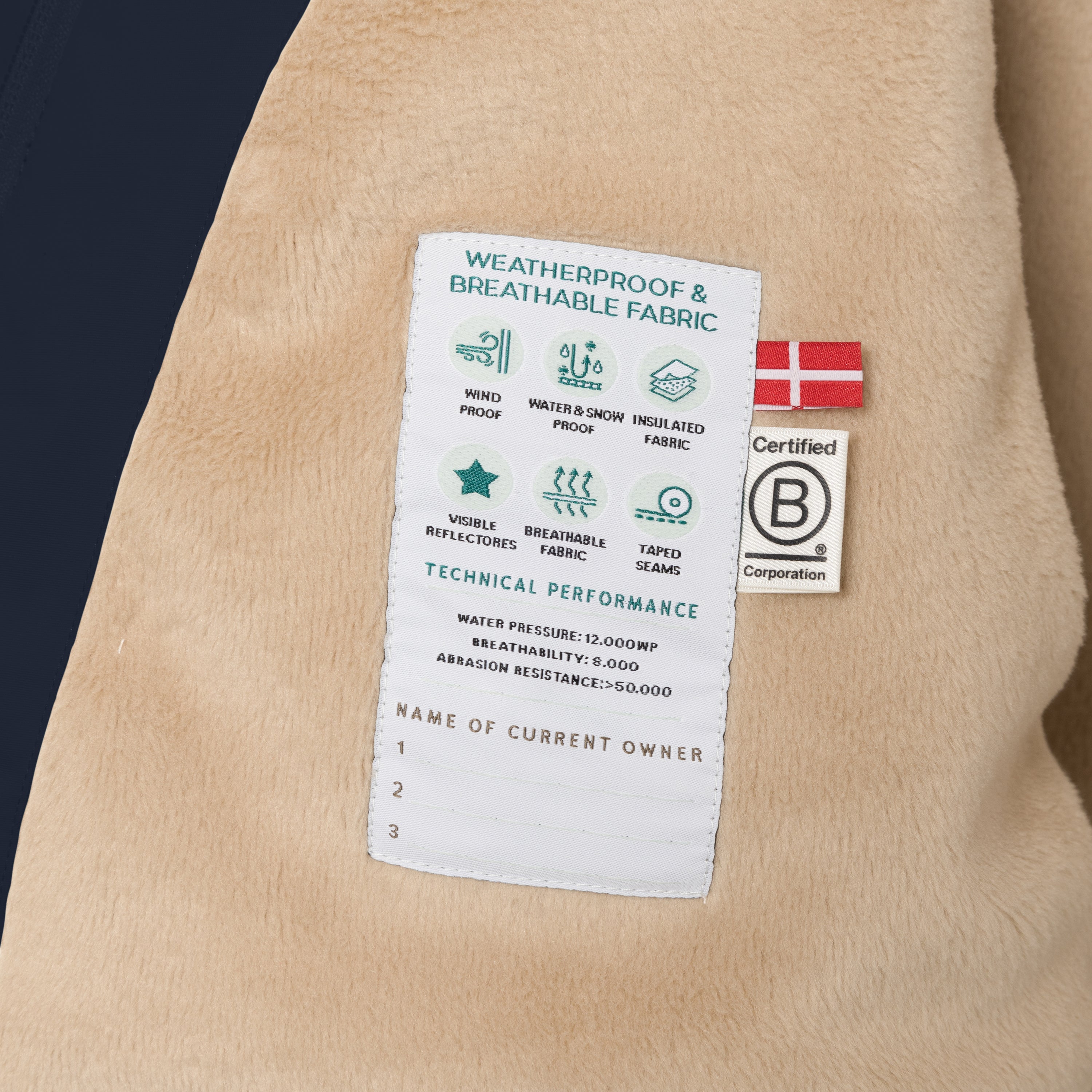 Internal technical label of the MATWANG fleece lined winter jacket sewn into the beige fleece lining, displaying windproof, water and snow proof, insulated fabric, visible reflectors, breathable fabric and taped seams icons, 12,000 water pressure rating, 8,000 breathability, abrasion resistance above 50,000, Danish flag, B Corp certification logo, and three numbered spaces for recording current owner details.