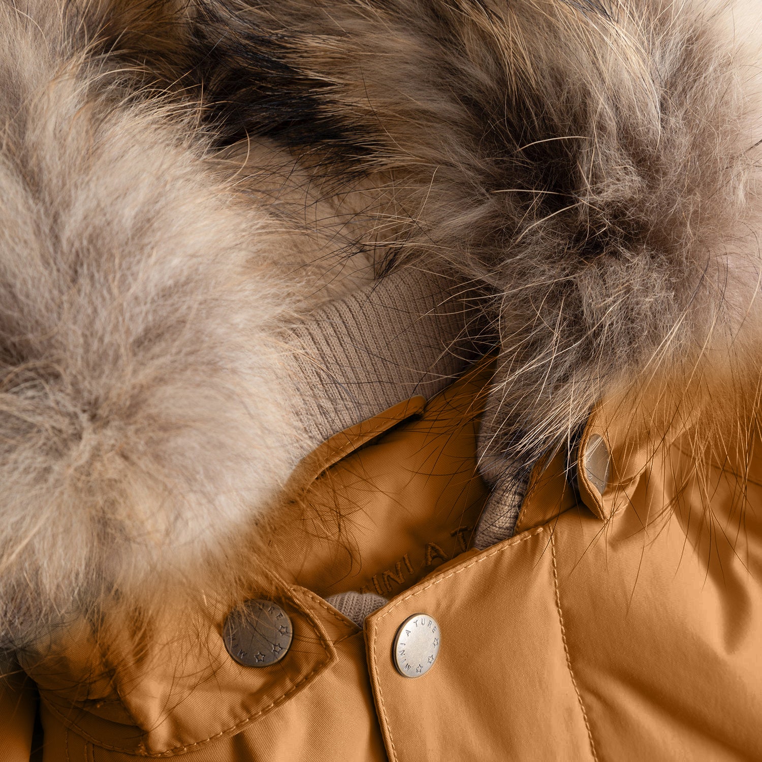 Close-up of the MATWALLY fleece lined winter jacket's detachable real fur hood trim showing the natural tones and texture of the fur against the warm caramel brown outer shell, with the branded press-stud fastening and soft beige fleece lining visible at the collar.