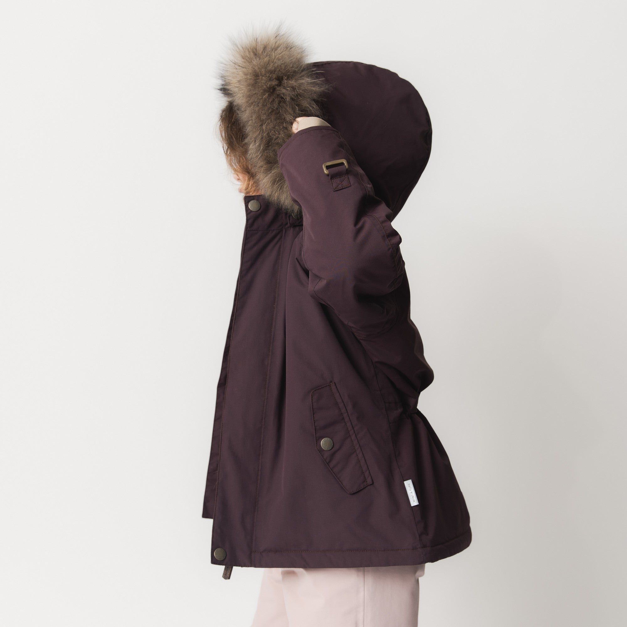 Young child wearing the MATWALLY fleece lined winter jacket in deep burgundy, shown in profile with the detachable real fur hood trim raised, demonstrating the hood's generous coverage and the jacket's protective fit during cold-weather wear.