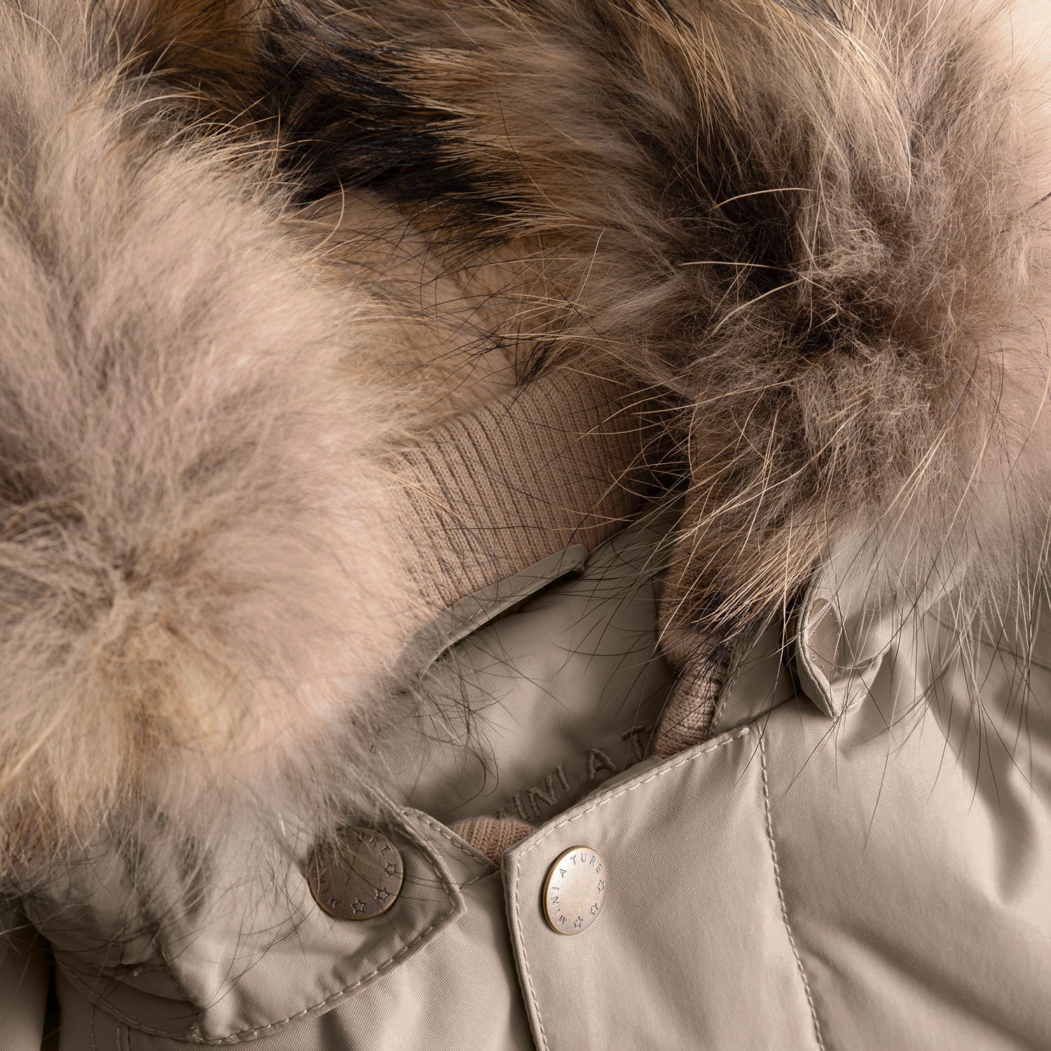 Close-up of the MATWALLY fleece lined winter jacket's collar in warm taupe, showing the natural multi-tonal real fur trim with fine, flowing texture, branded MINI A TURE press studs securing the detachable hood, and the beige ribbed collar visible beneath the fur alongside the hidden zip attachment mechanism.