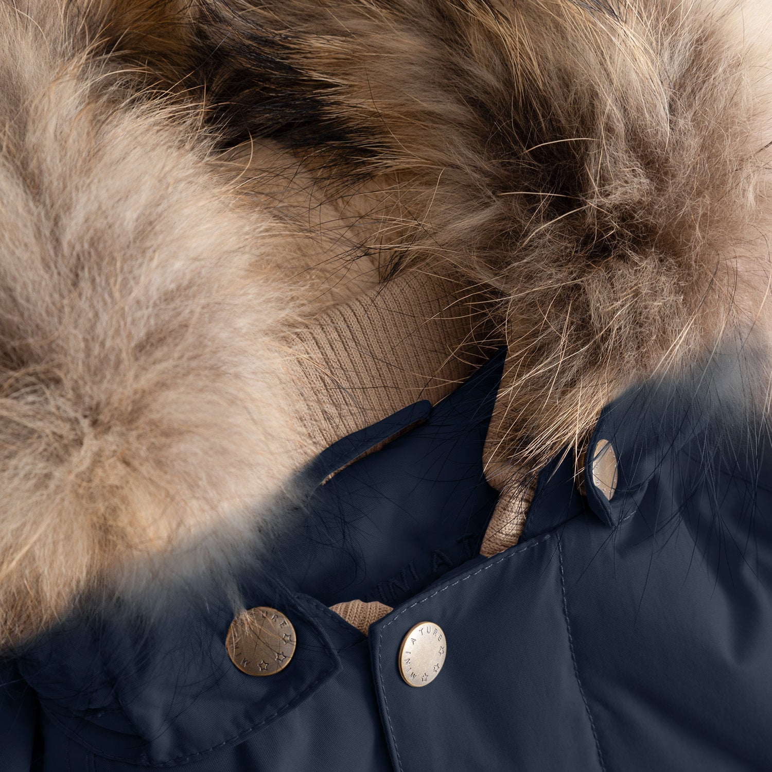 Close-up of the MATWALLY fleece lined winter jacket's collar in deep navy blue, showing the detachable real fur trim secured by branded MINI A TURE press studs, with the natural multi-tonal fur displaying soft, layered texture above the beige ribbed collar and the hidden zip mechanism beneath.