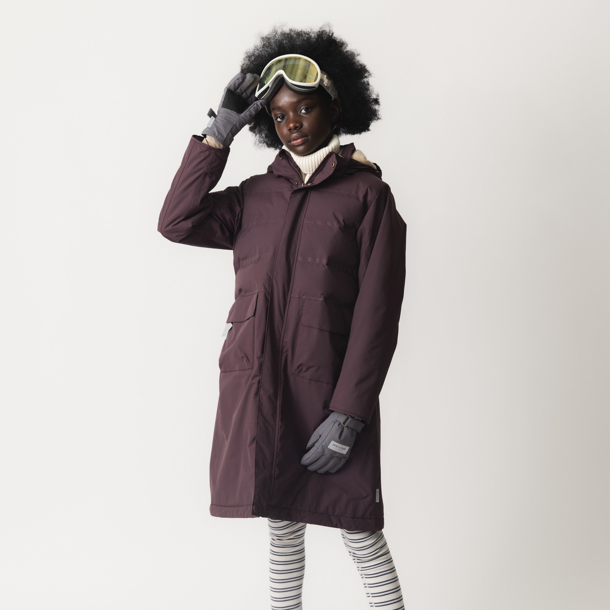 MATVENCASIA fleece lined winter jacket in deep burgundy, shown with ski goggles and gloves, demonstrating the extended length and detachable hood designed for older children.