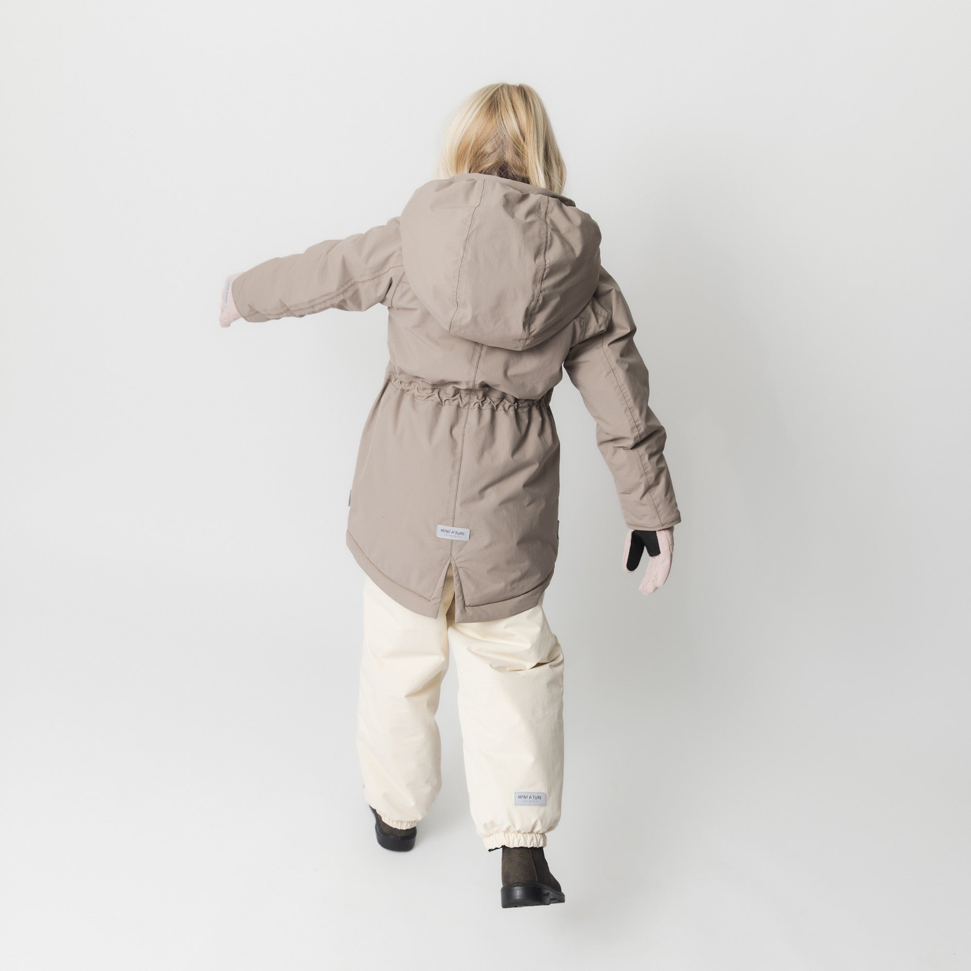 MATVIKANIA fleece lined winter jacket in taupe worn by a child in motion, demonstrating the improved sleeve fitting and snow cuffs with thumb openings that allow full arm movement during active play.