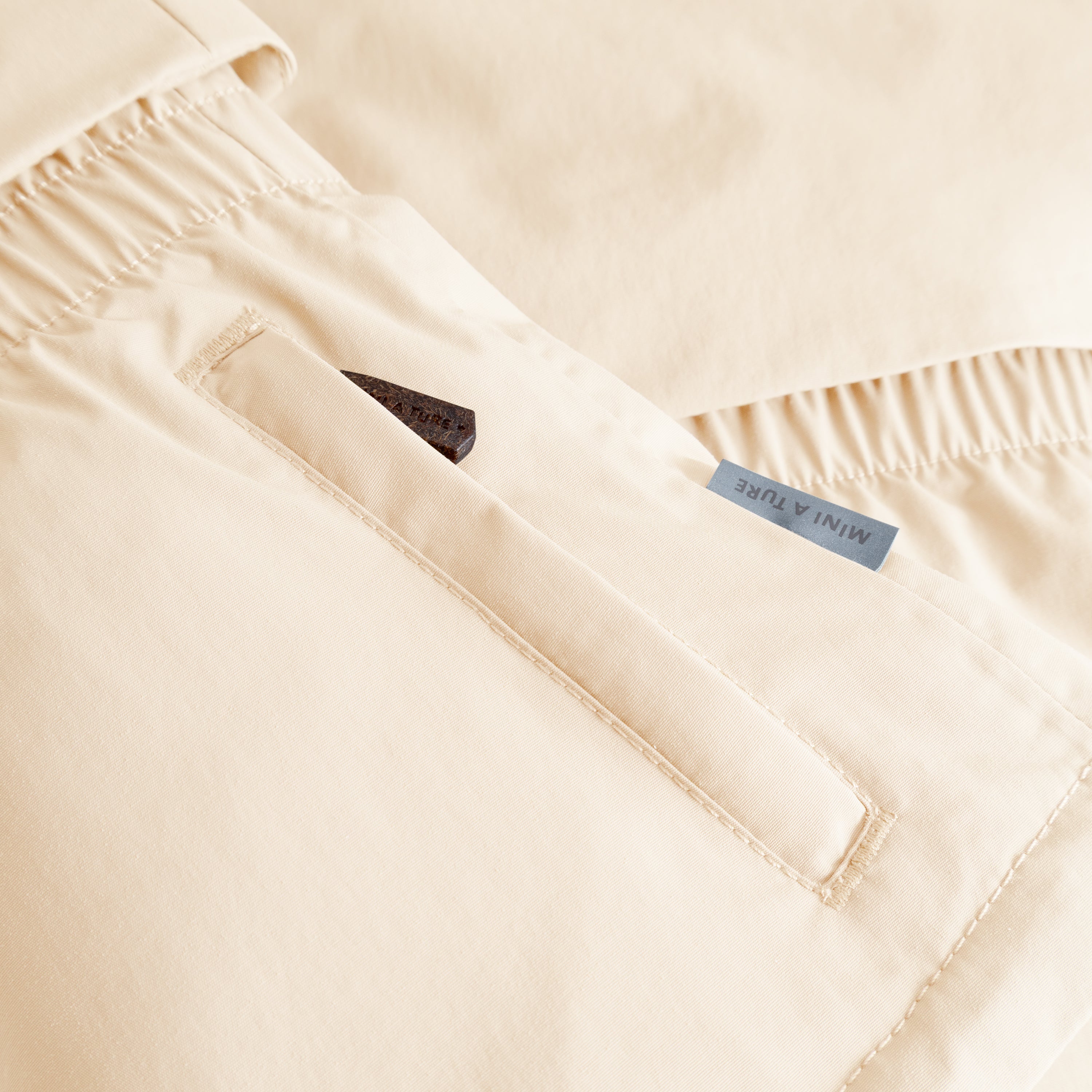 MATALGEANA winter jacket detail in cream showing the right front zip pocket with 70 lux reflective star zipper pull partially visible, elasticated waist panel with gathered stitching, and the waterproof recycled polyamide shell with beige fleece lining.