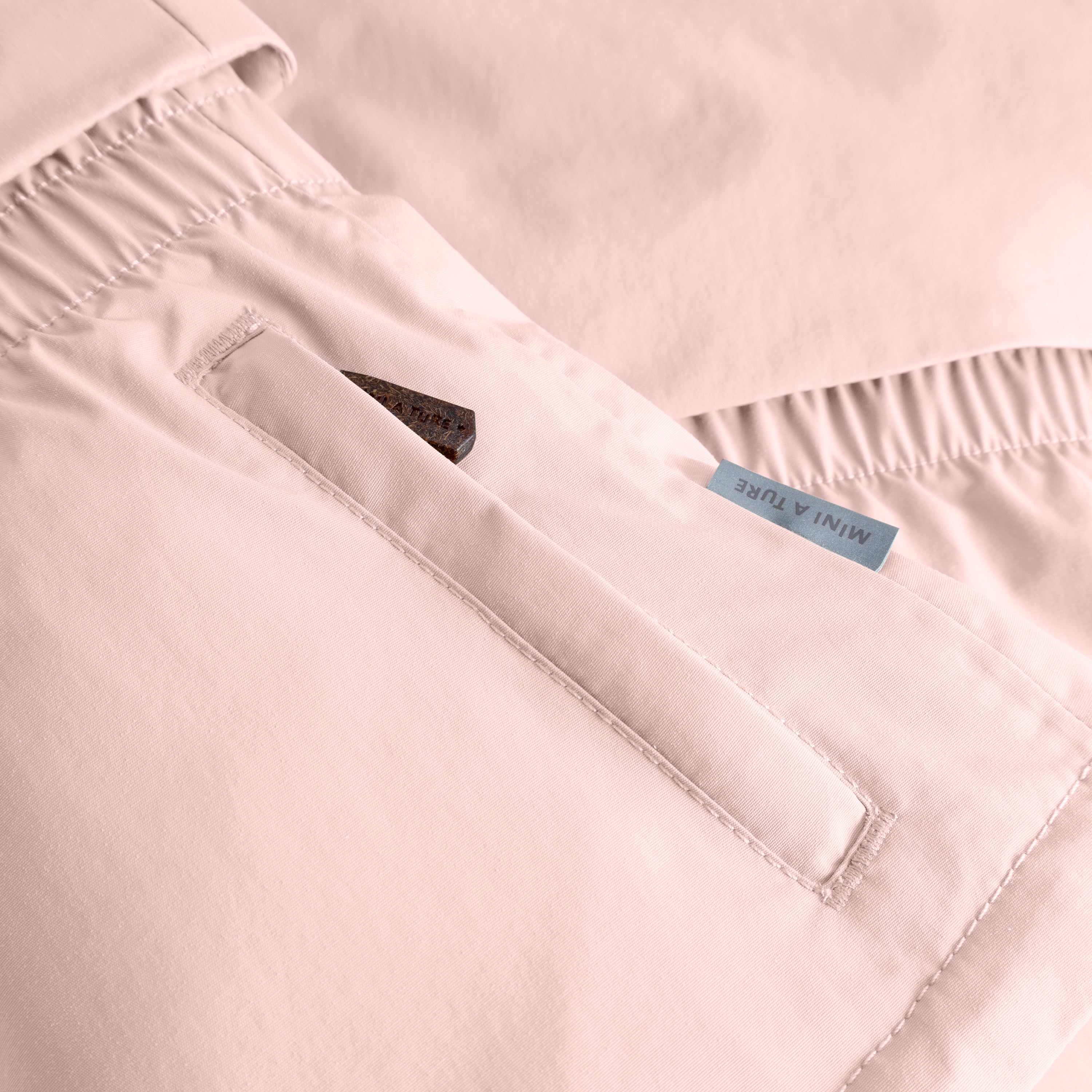 MATALGEANA winter jacket detail in soft pink showing the right pocket with reflective star emblem, MINI A TURE woven label, elasticated waist section with gathered stitching, and the waterproof recycled polyamide shell construction.