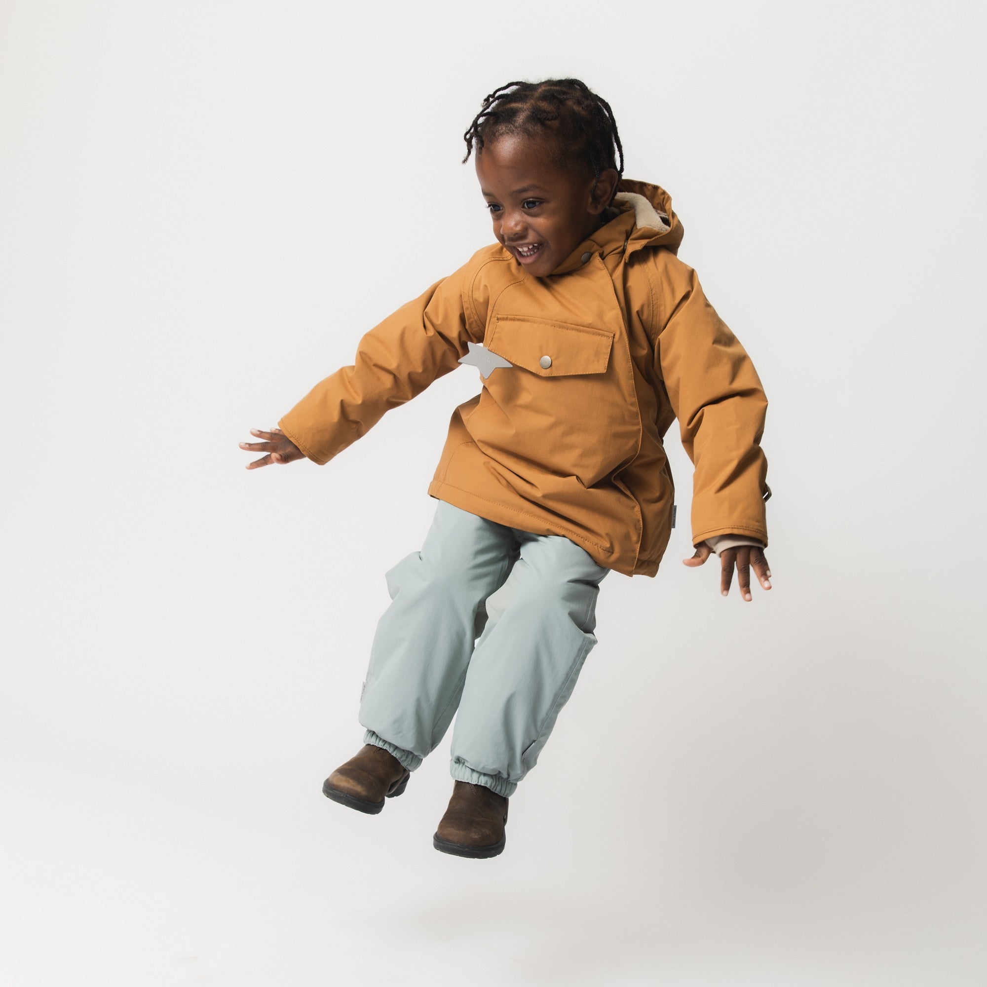 MATWALENTEX snow pants in pale mint green worn by a child mid-jump, paired with a caramel jacket and brown boots, demonstrating the dropped crotch design and unrestricted freedom of movement during active play.