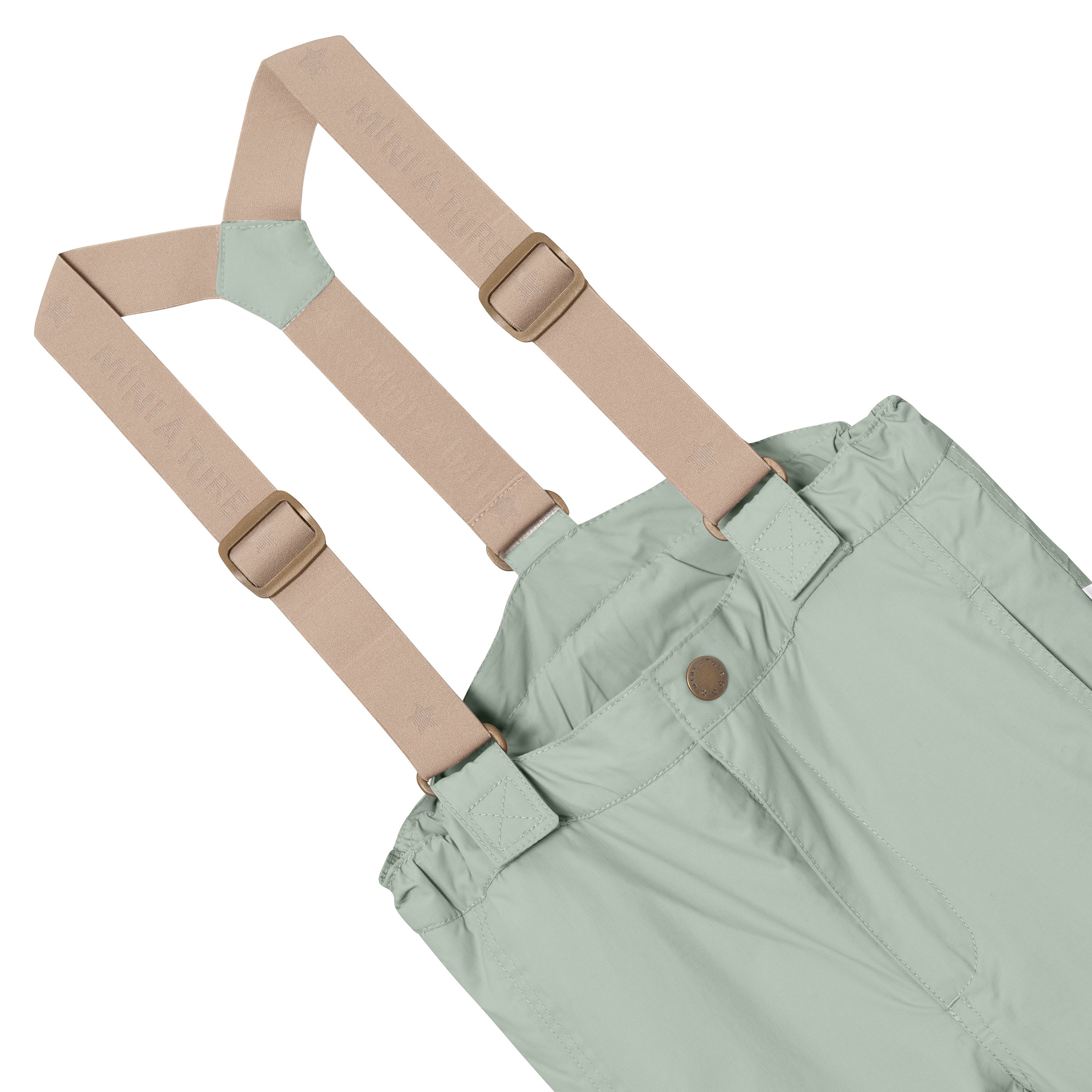 MATWITTE snow pants in pale sage green showing the front waistband detail with snap-button closure, elasticated waist and the removable beige elastic suspenders with metal slider adjusters threaded through fabric loops at the front.
