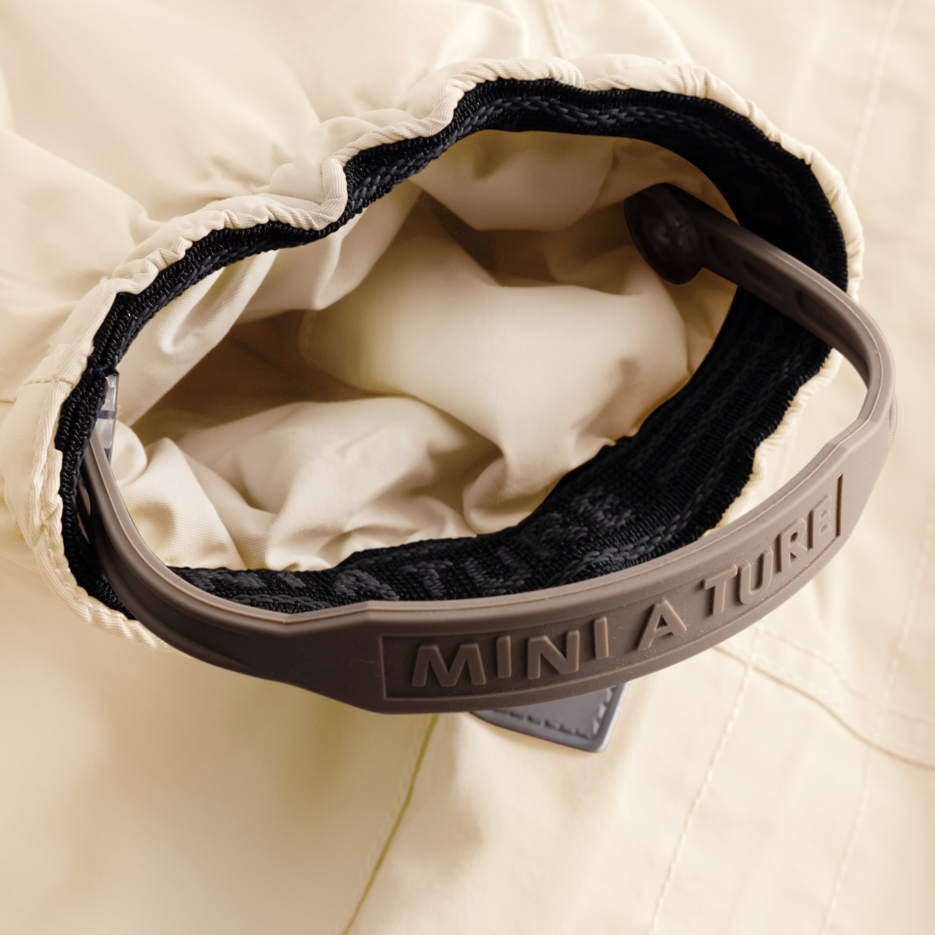 Close-up of the MATWISTI fleece lined snowsuit in warm beige showing the internal adjustable waist with black elasticated drawstring and embossed MINI A TURE branding on the grey plastic cord lock, with beige fleece lining visible inside.