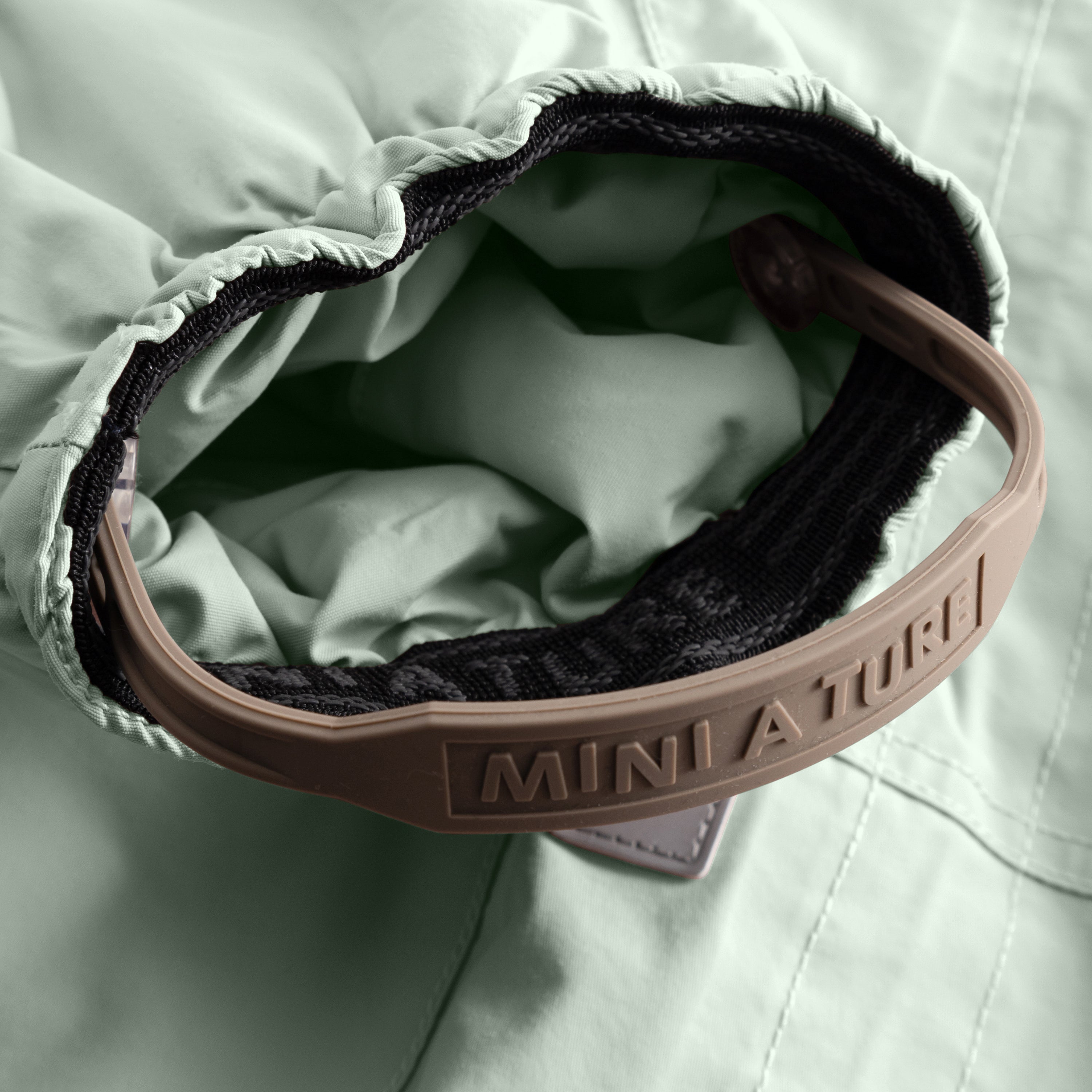 Interior view of the MATWISTI fleece lined snowsuit in sage green, highlighting the soft fleece lining, elasticated waist adjustment and MINI A TURE branded foot strap detail.