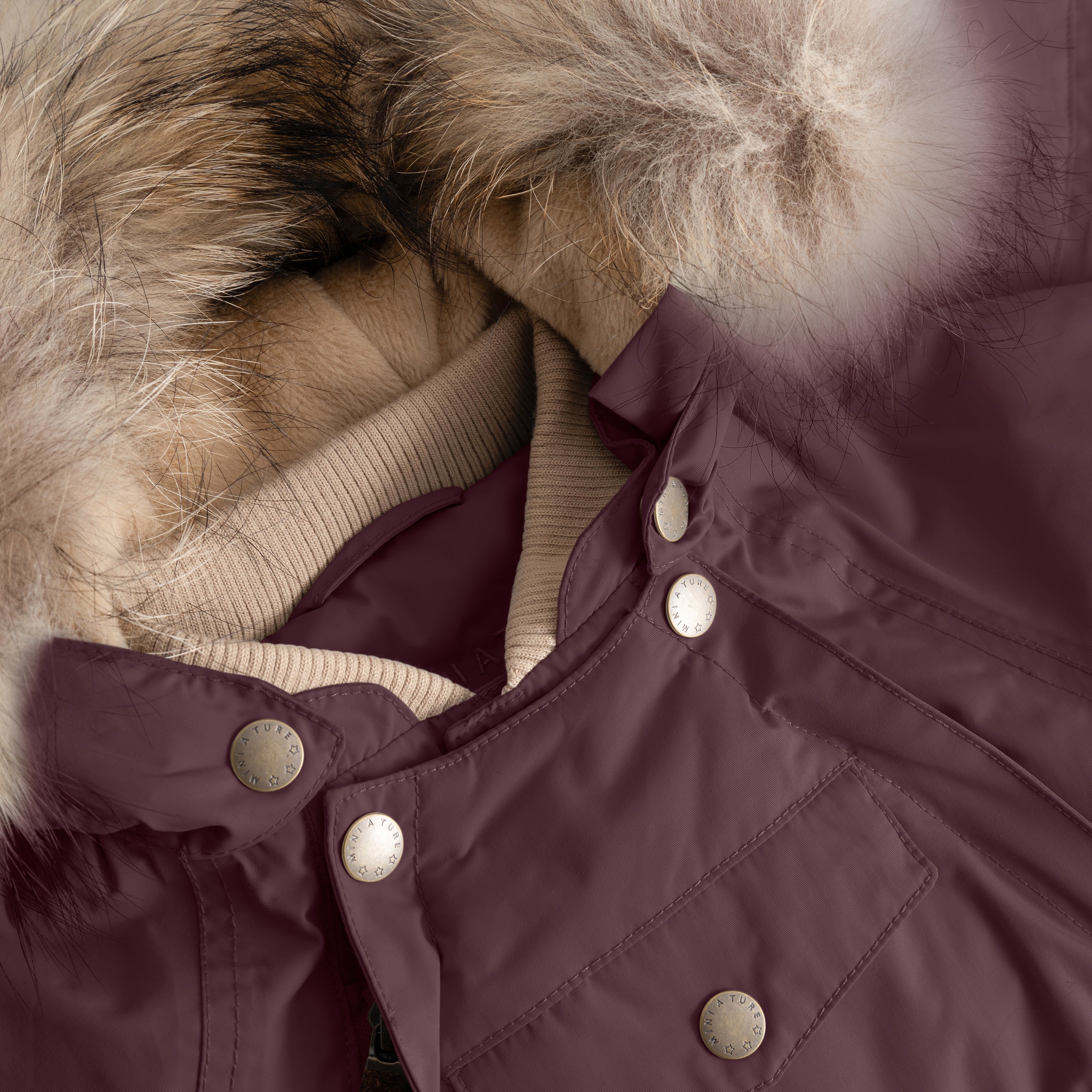 Close-up of MATWISTI fleece lined snowsuit fur in deep burgundy showing the detachable genuine fur hood trim, taupe ribbed collar, MINI A TURE branded press-stud fastenings along the chest, and front pocket detail on the waterproof shell.