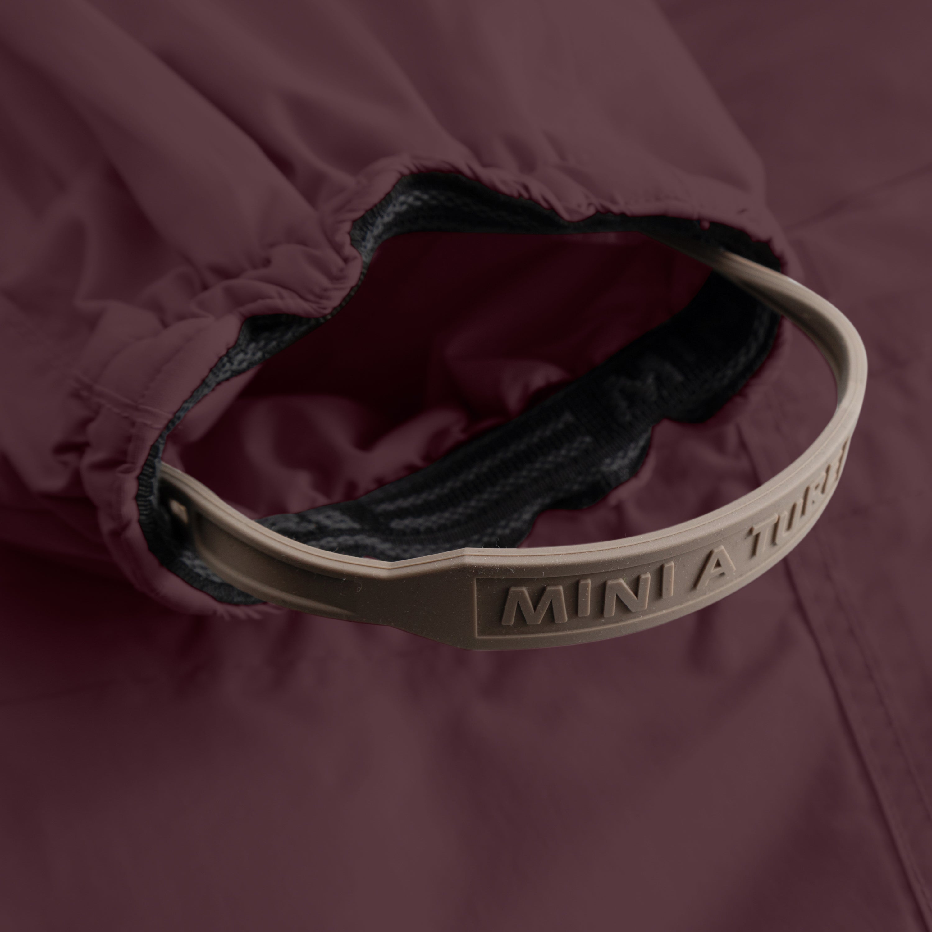 Detail of MATWISTI fleece lined snowsuit fur in deep burgundy showing the internal adjustable waist with embossed MINI A TURE branding on the taupe elastic strap, contrasting with the dark fleece lining and burgundy waterproof outer shell.
