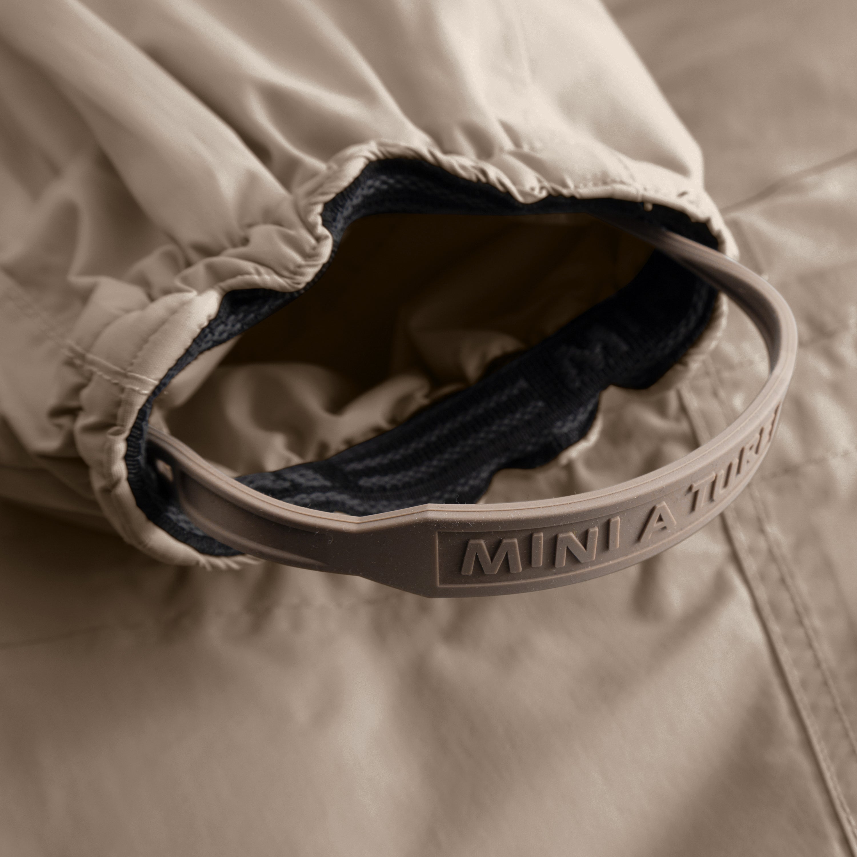 Detail of MATWISTI fleece lined snowsuit fur showing the internal adjustable waist with embossed MINI A TURE branding and the contrast between the taupe outer shell and dark fleece lining.