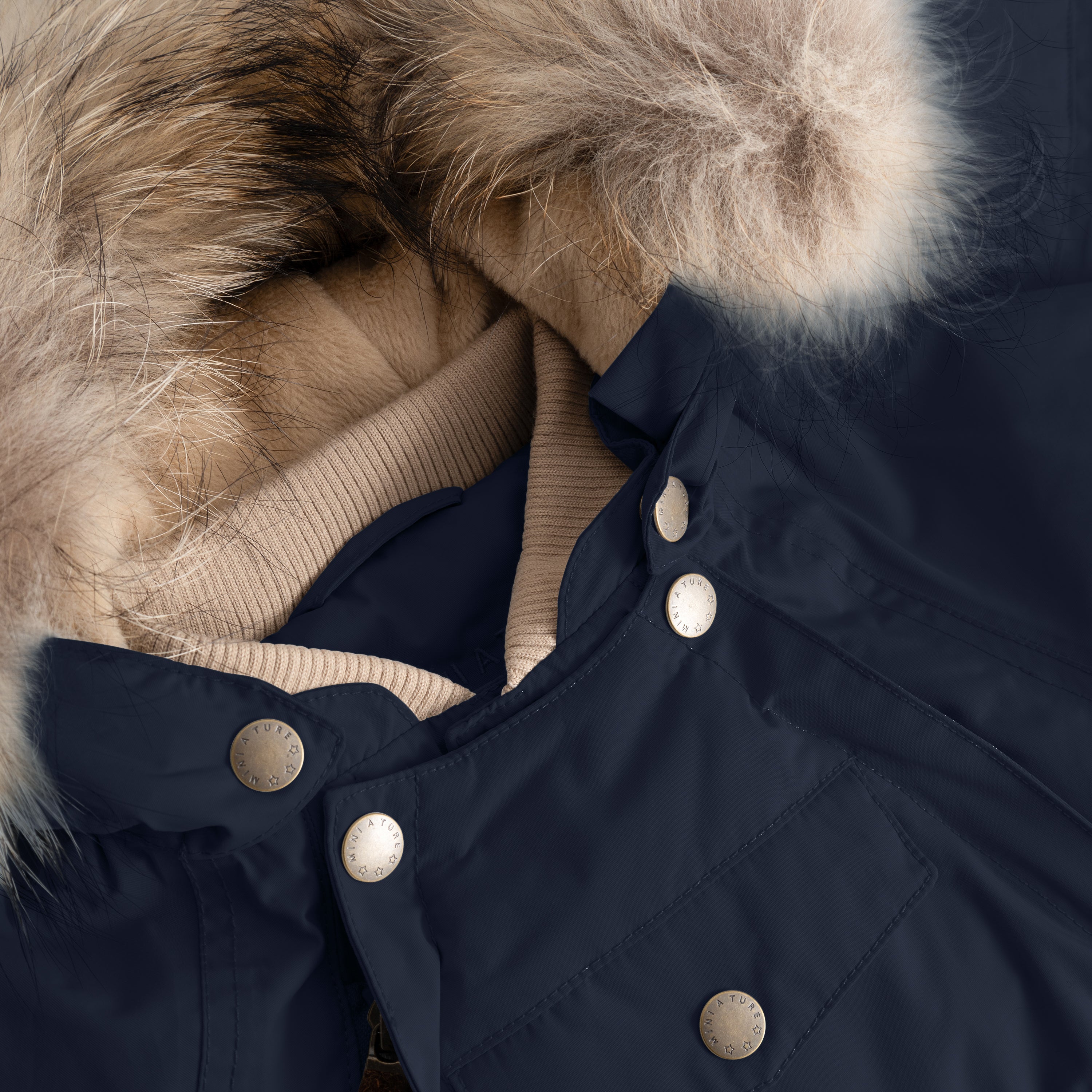 Close-up of MATWISTI fleece lined snowsuit fur in navy blue showing the genuine fur hood trim, taupe ribbed collar, MINI A TURE branded press-stud fastenings along the chest, and front pocket detail on the waterproof shell.