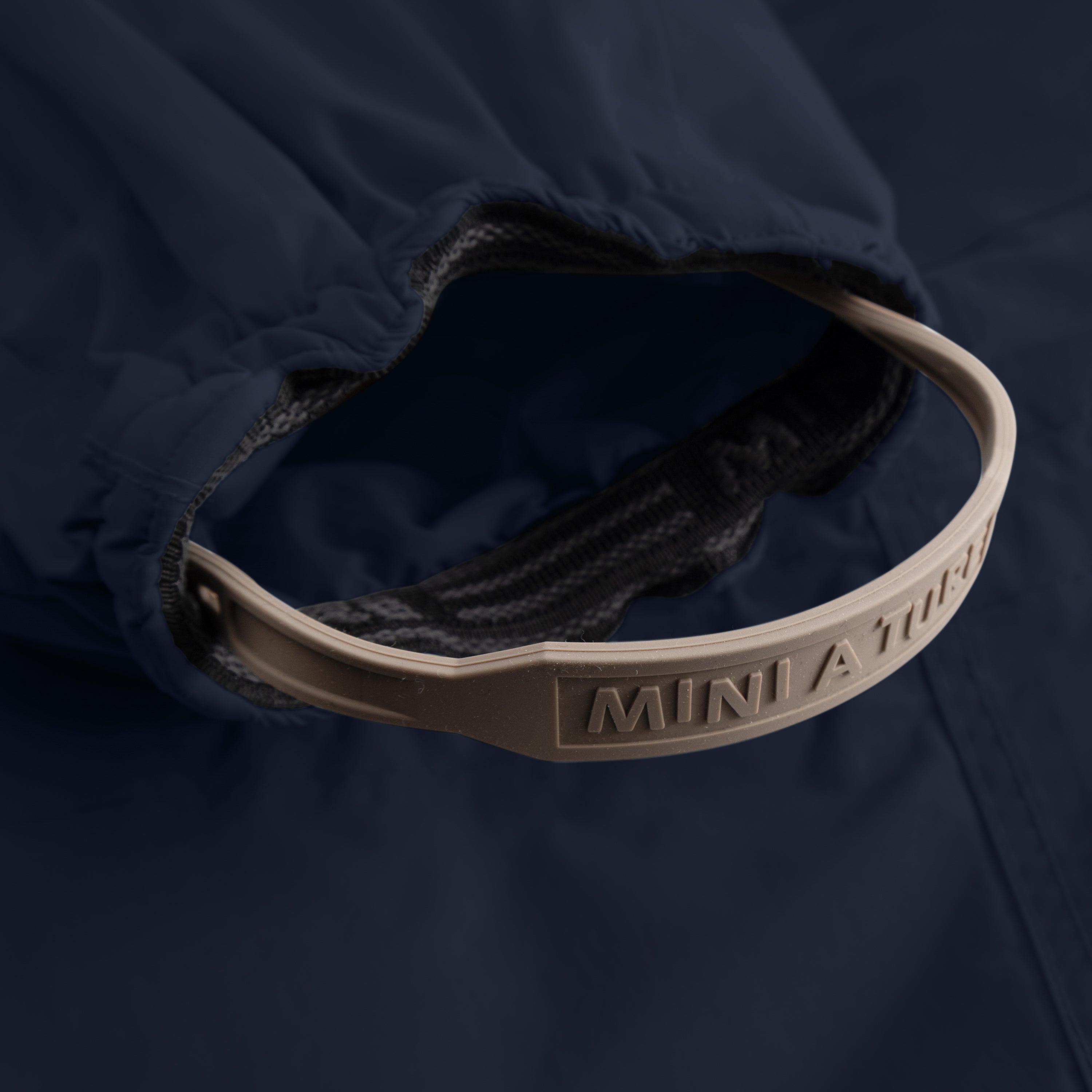Detail of MATWISTI fleece lined snowsuit fur in navy blue showing the adjustable and detachable foot strap with embossed MINI A TURE branding on the taupe silicone band, elasticated ankle cuff with dark fleece lining, and beige fleece interior visible against the waterproof outer shell.