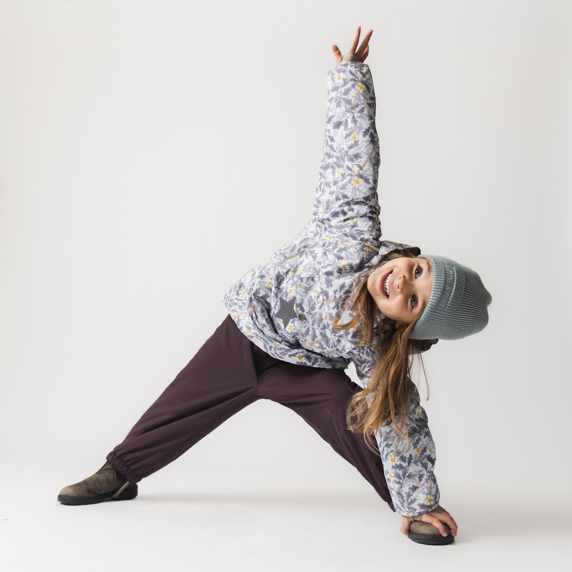 MATWANG fleece lined winter jacket worn by a child in an active play pose, demonstrating the jacket's freedom of movement through the Scandinavian floral print shell, paired with dark trousers and a grey knitted beanie.